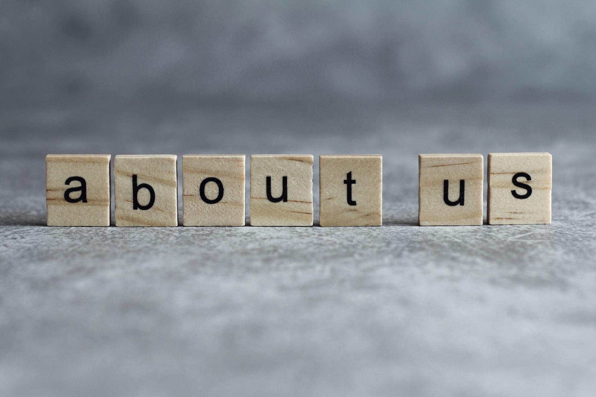 About us word written on wood cube with gray background.